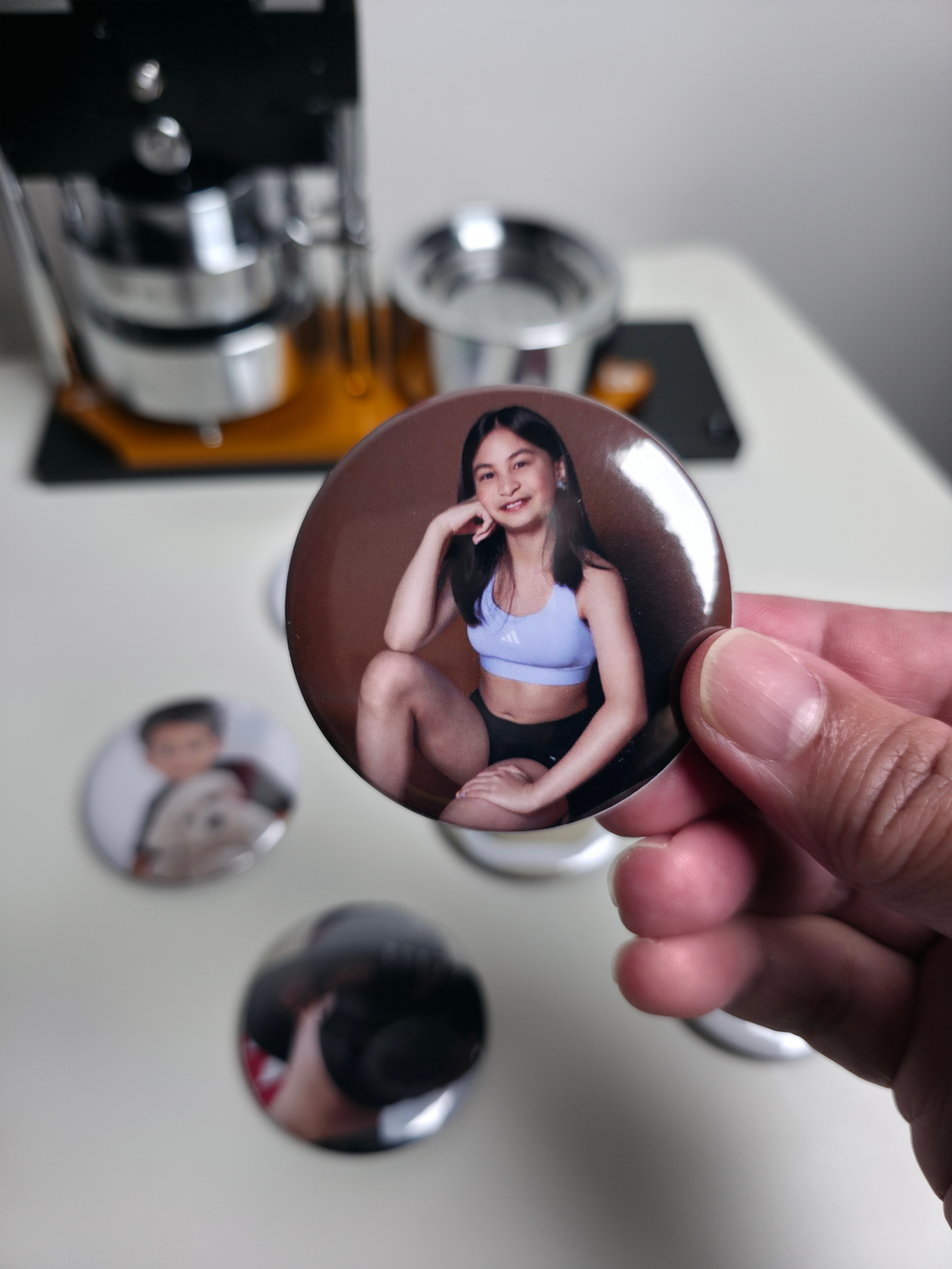 Person holding a button with a photo of a girl with other photo magnets.
