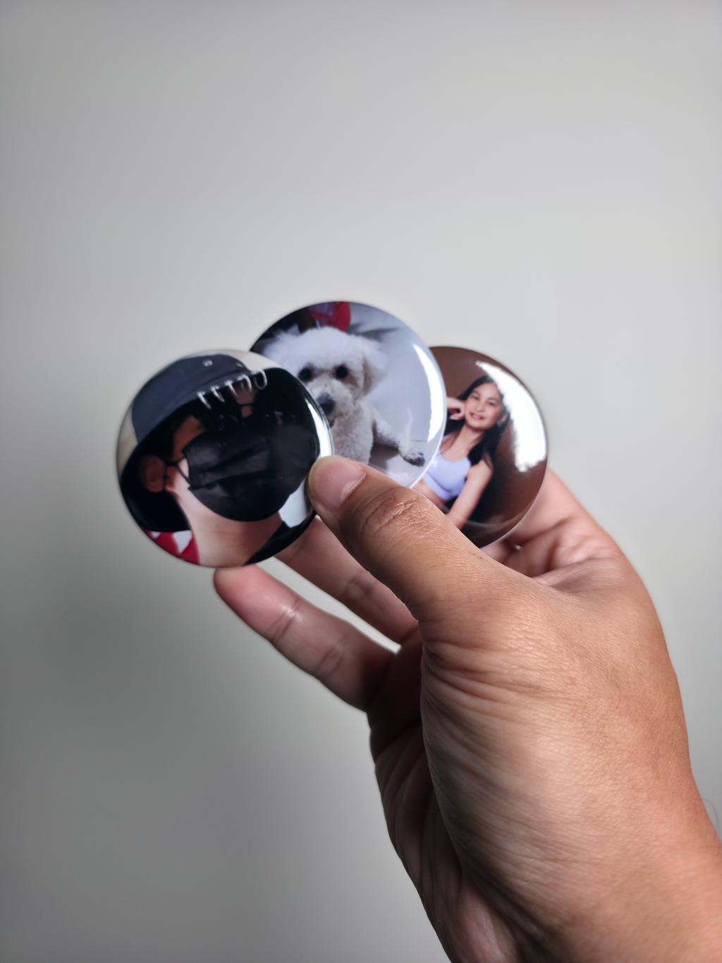 Hand holding round photo magnets with images of a person, a dog, and another person on its surface.