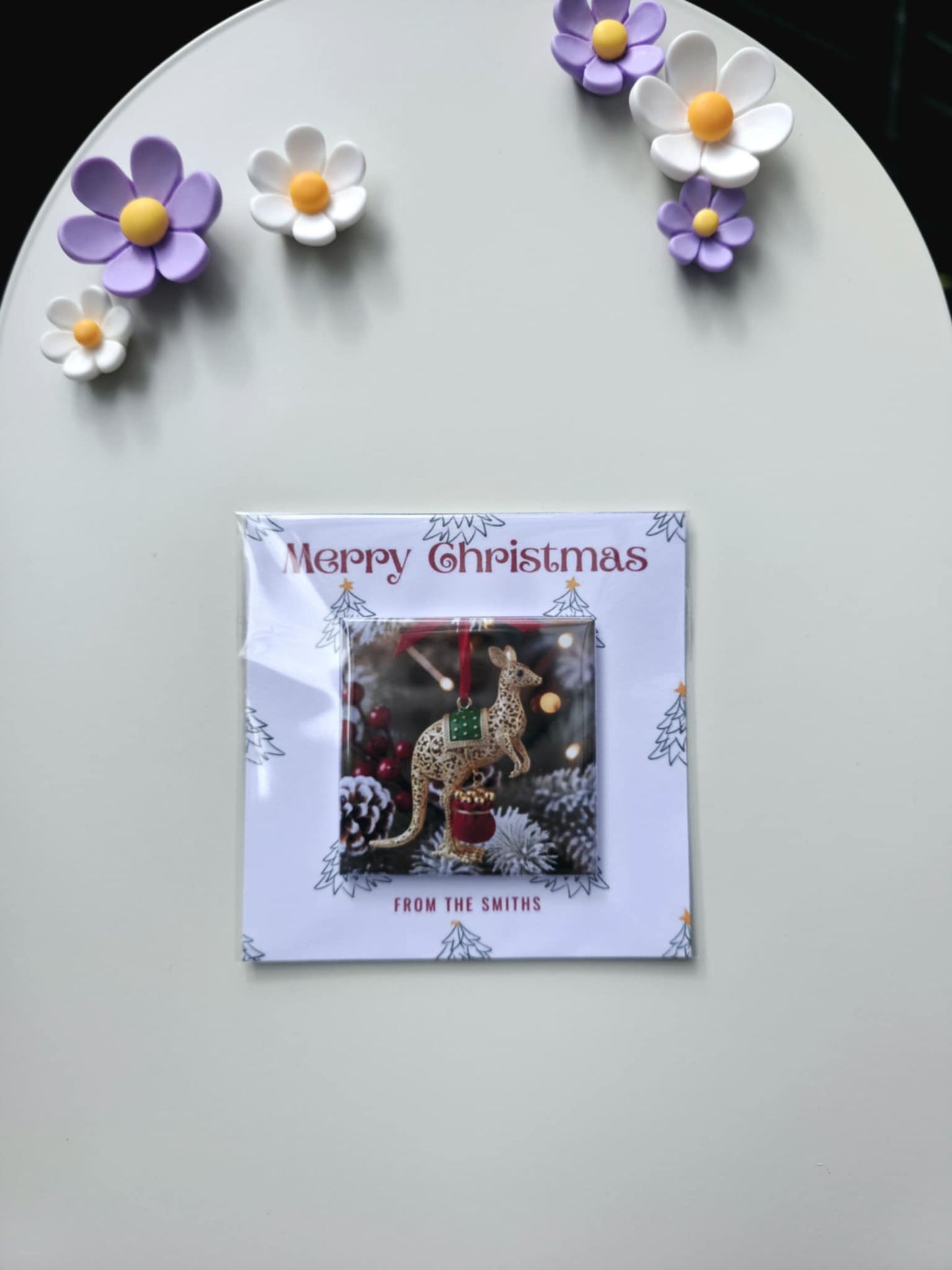 Christmas card with reindeer ornament on a decorative surface with flowers.