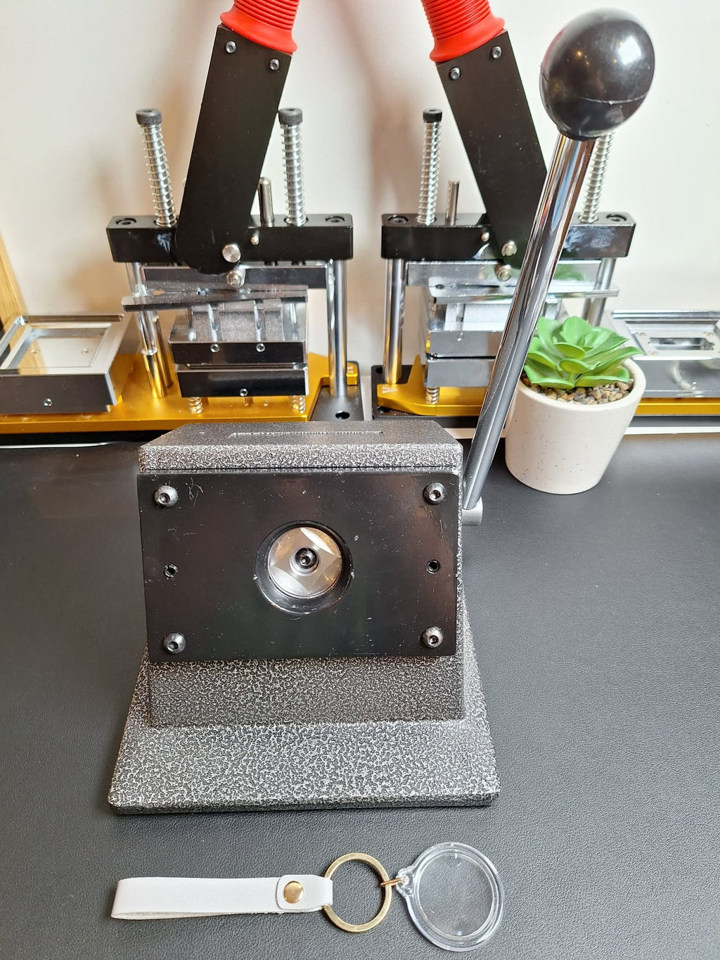 Metal stamping machine on a gray surface with a keychain and blank tag in front