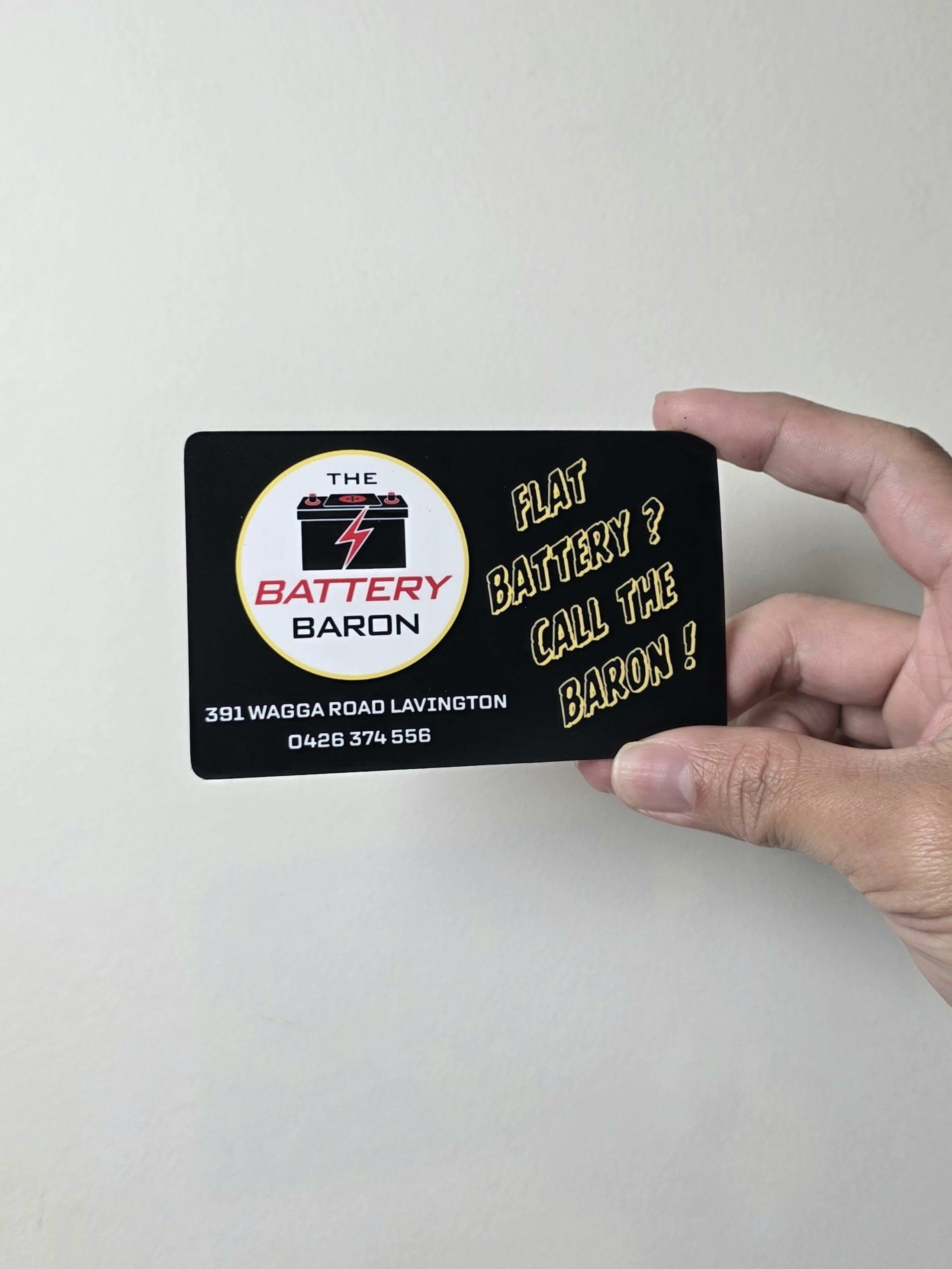 Hand holding a card with 'The Battery Baron' branding and contact information.