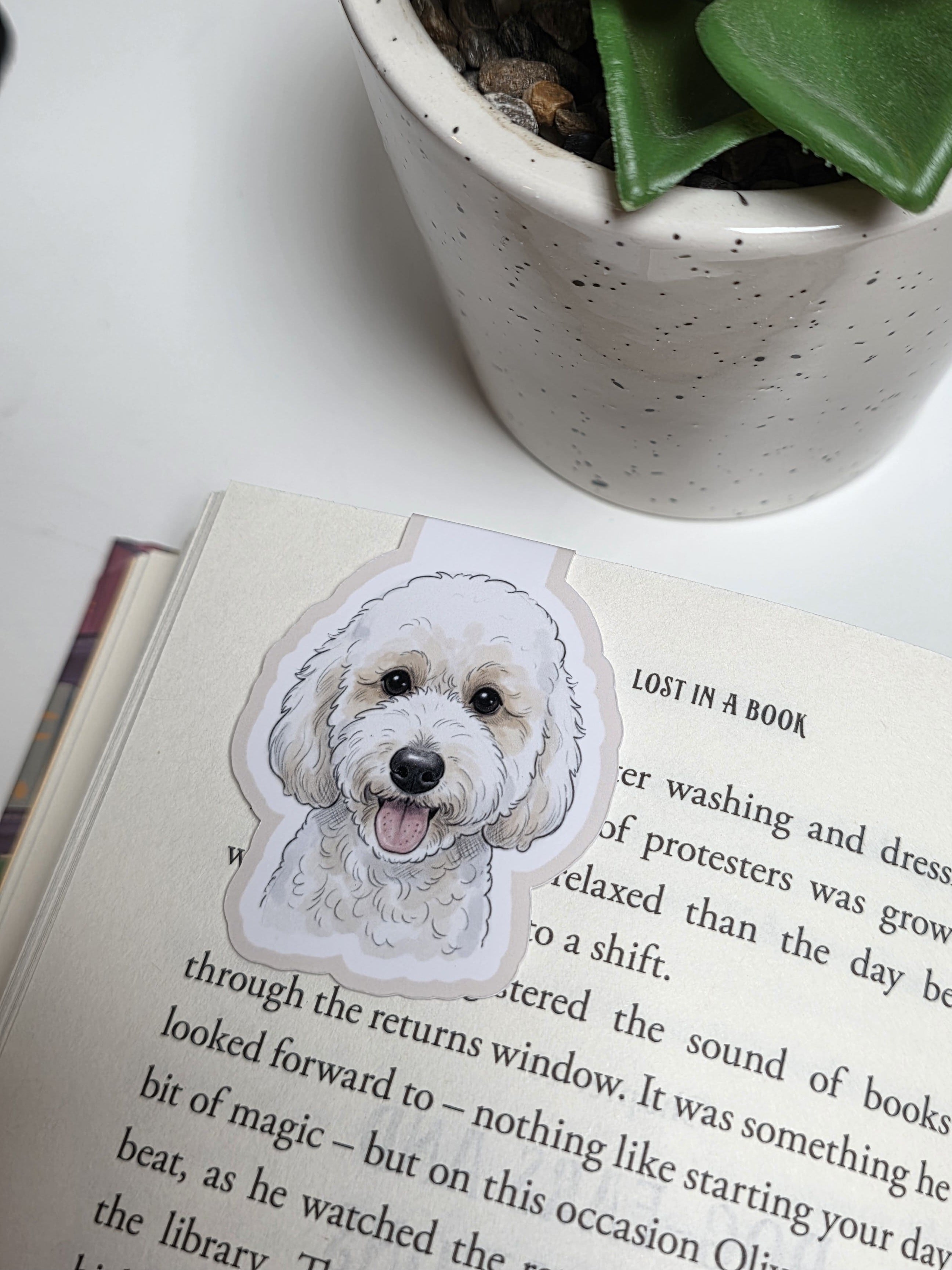 Book with a dog illustration on a white surface next to a potted plant