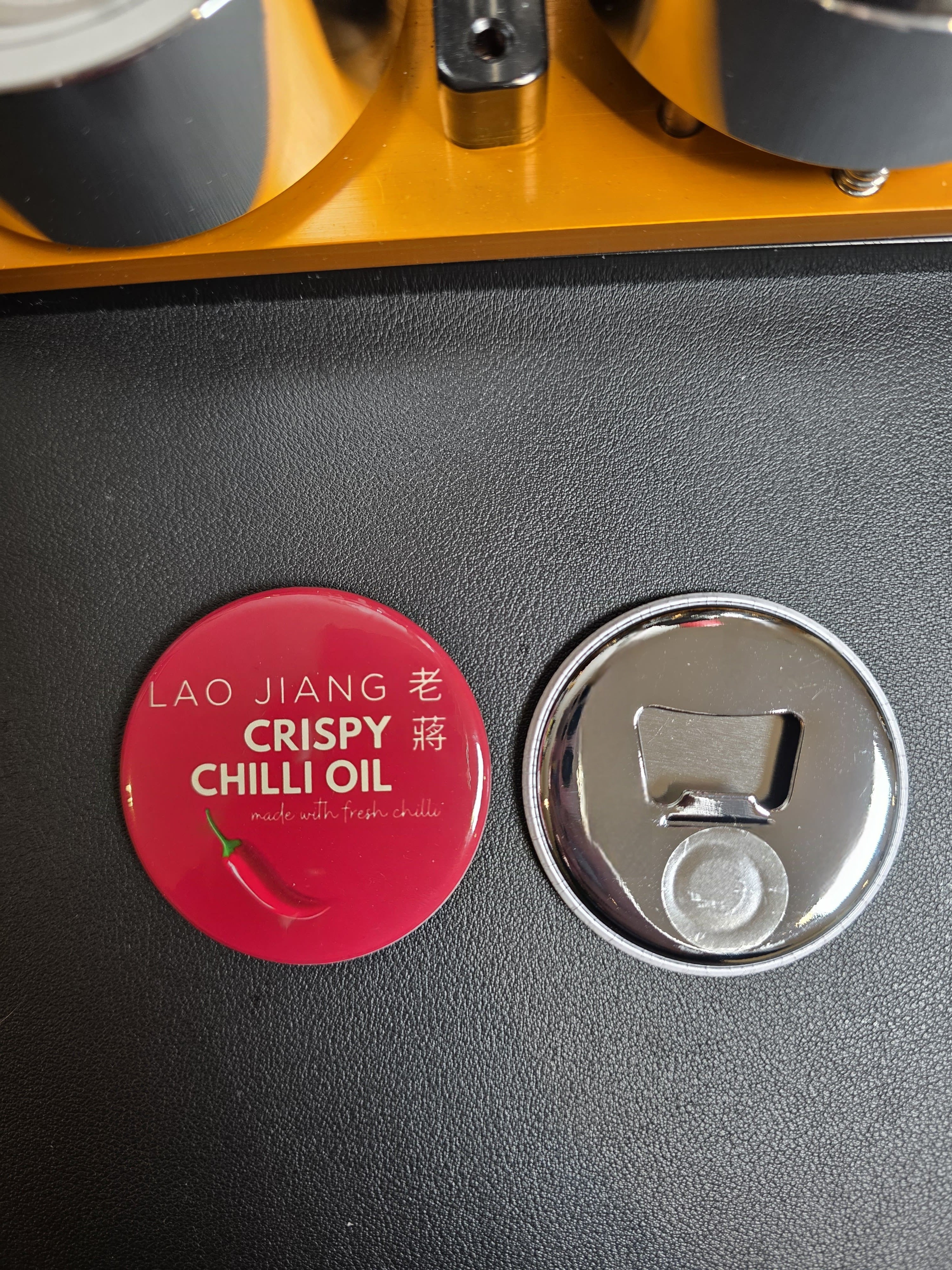 Lao Jiang Crispy Chilli Oil bottle cap on a black surface with a bottle opener.