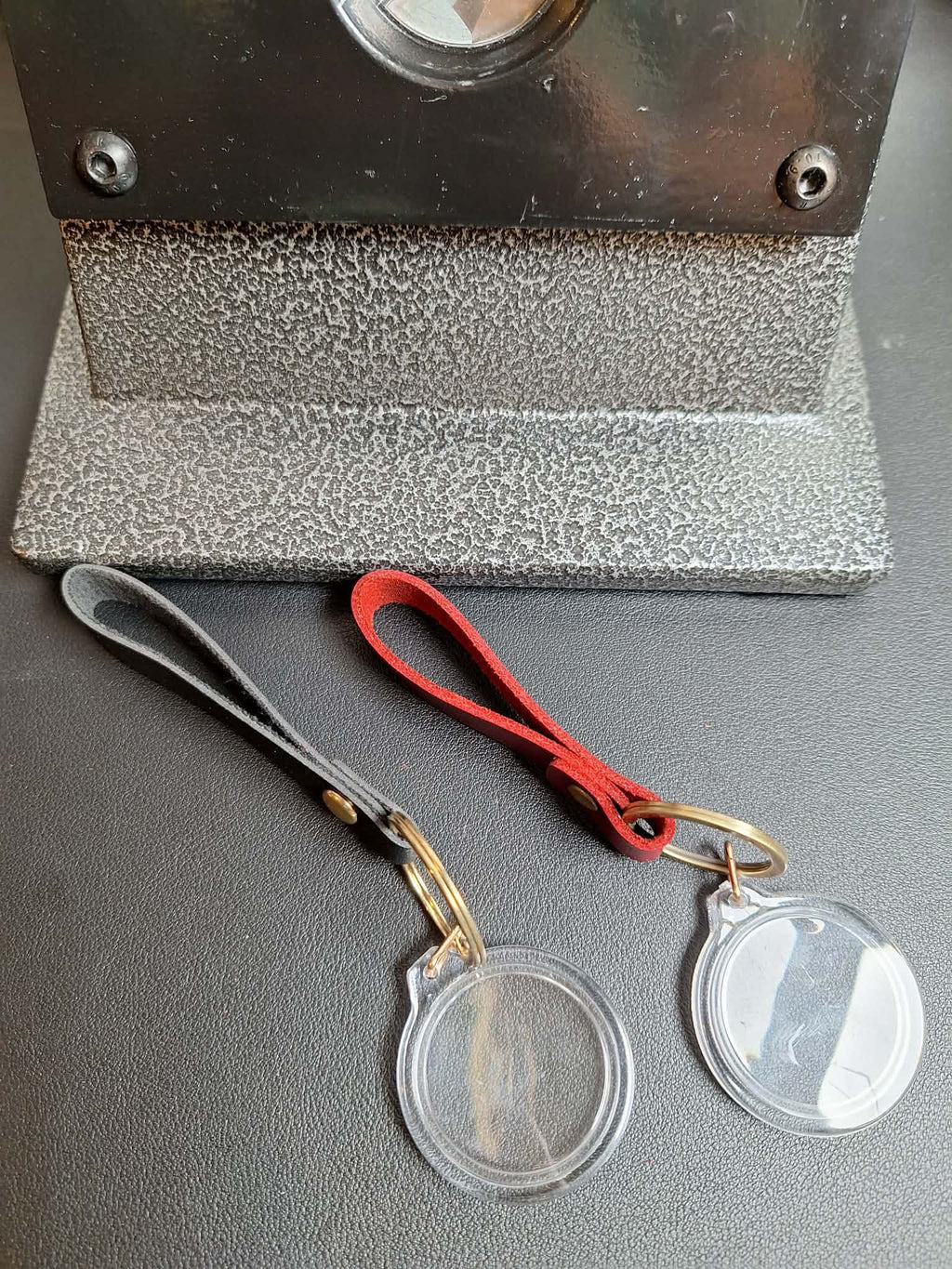 Two clear plastic coin holders with gold clasps on a gray surface, with a magnifying glass in the background.