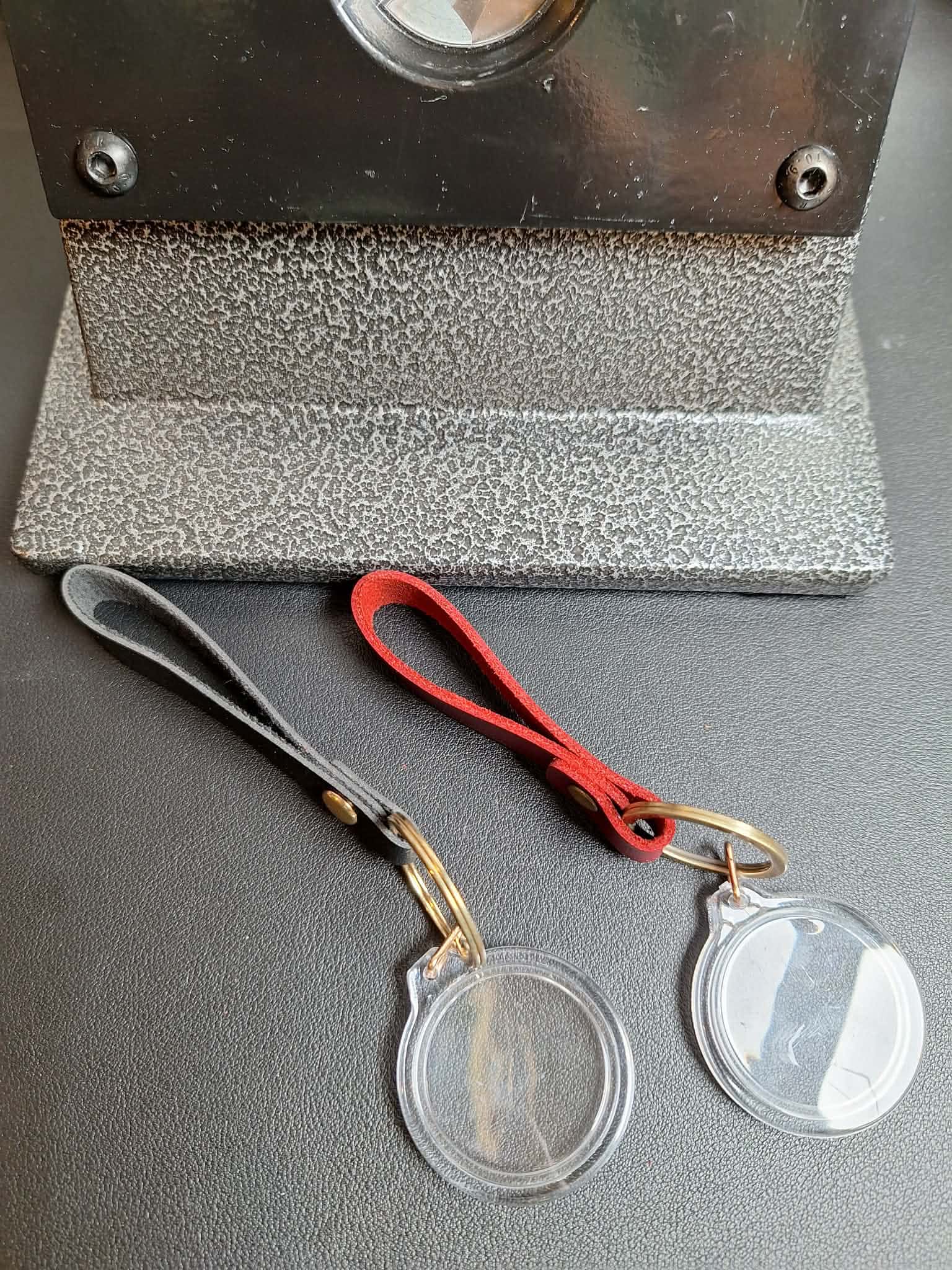 Two clear plastic coin holders with gold clasps on a gray surface, with a magnifying glass in the background.