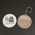 Compact mirror with a keychain and a round sticker labeled 'Joke photo magnets' on a dark surface.