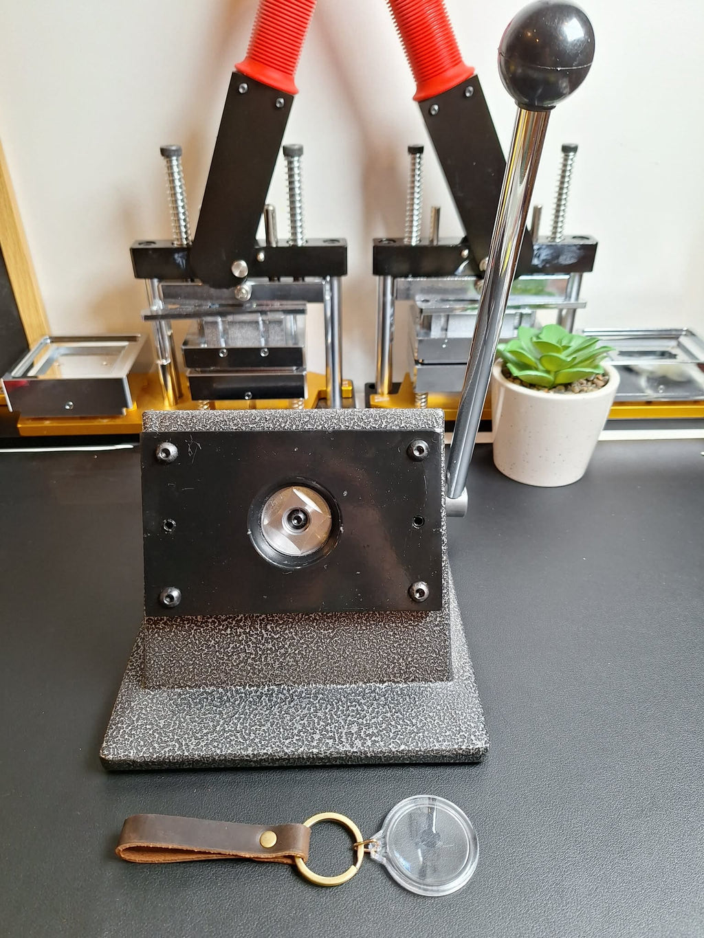 Metal stamping machine on a table with a plant and keychain in the background