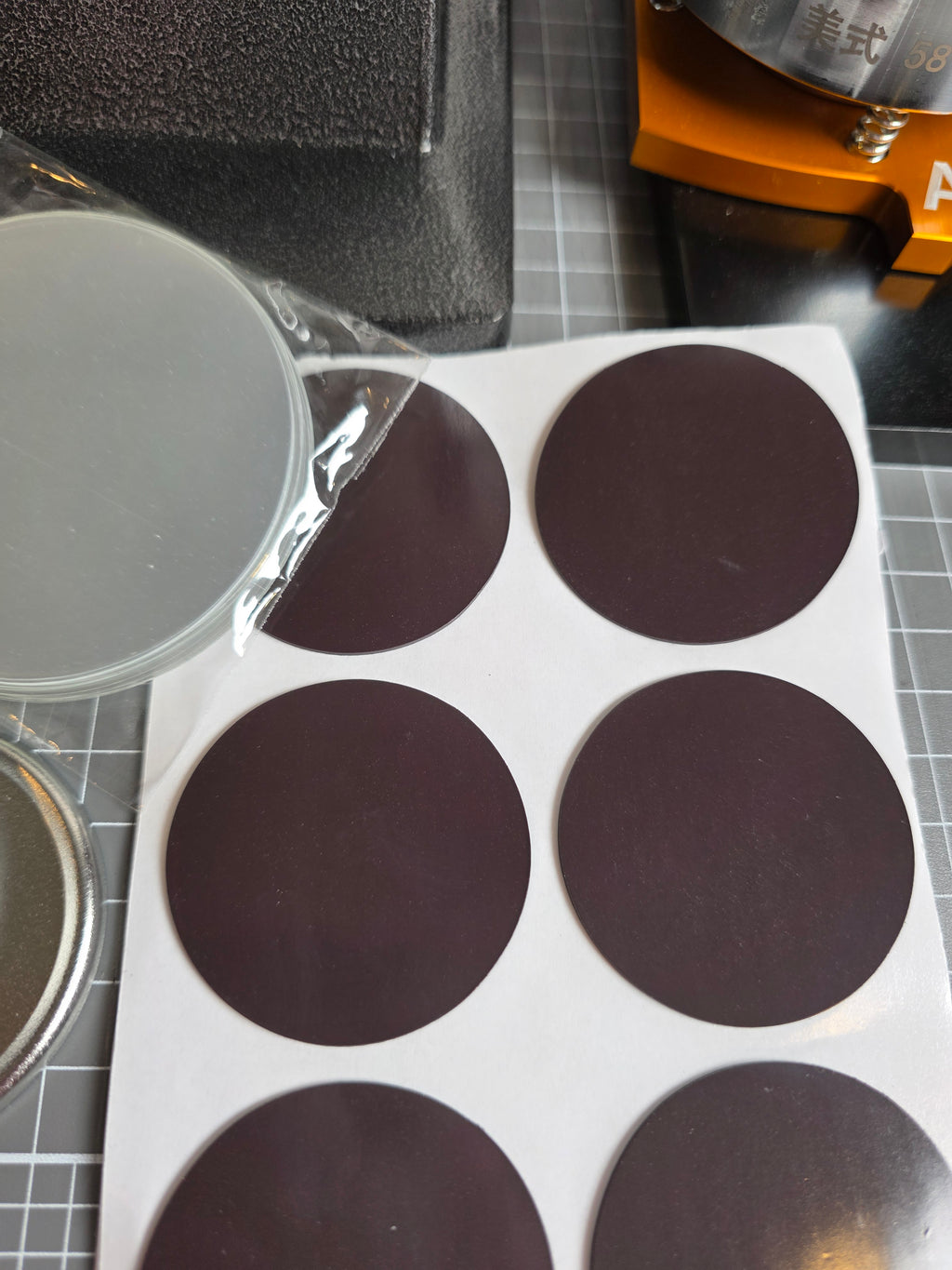 Sheet of round black adhesive pads on a white backing with a close-up of a single pad in the foreground.