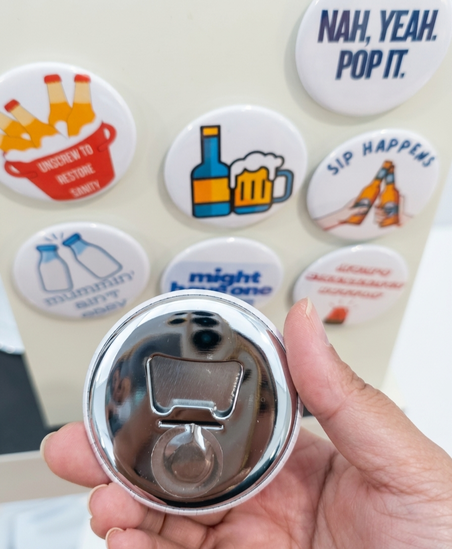 Metallic bottle opener with a hand holding it, surrounded by various buttons with different designs and text.