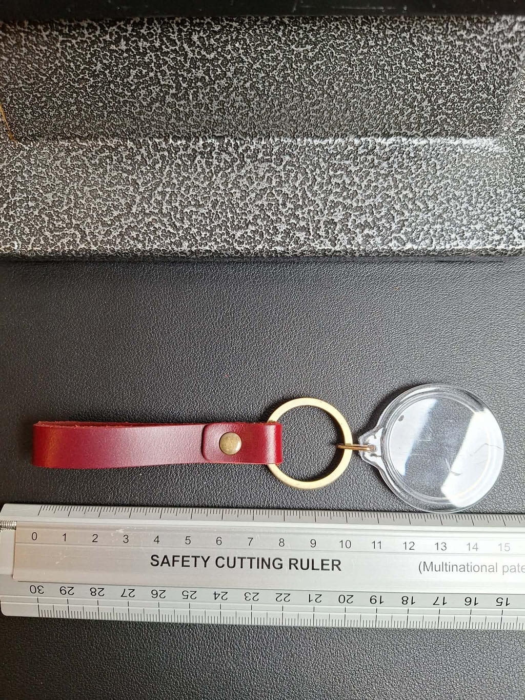 Red leather keychain with a magnifying glass on a gray surface with a ruler for scale.