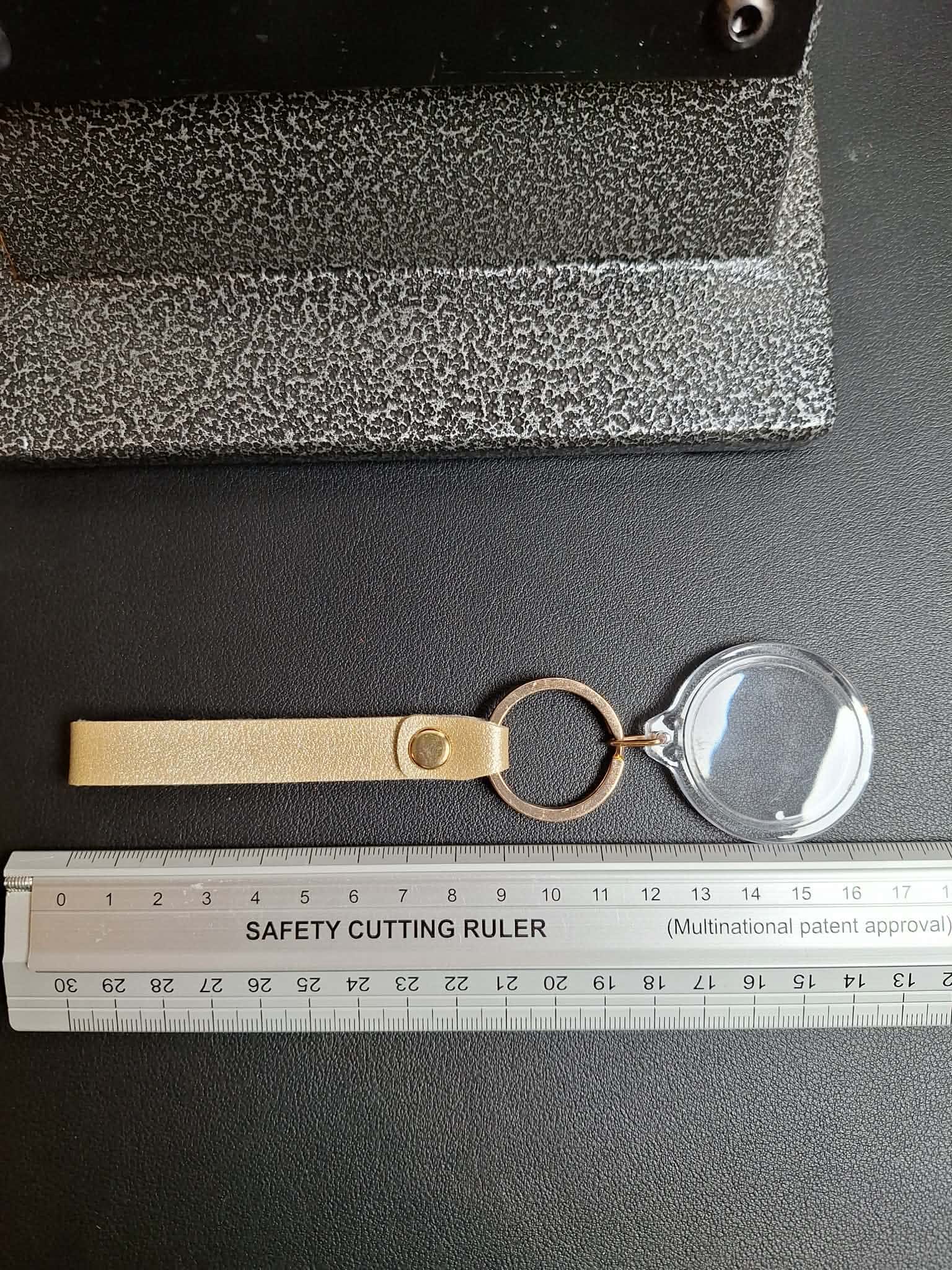 Keychain with magnifying glass and ruler for scale on a dark surface