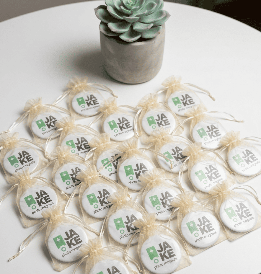 Round magnets with 'JAKE' branding on a white surface with a succulent plant in the background.