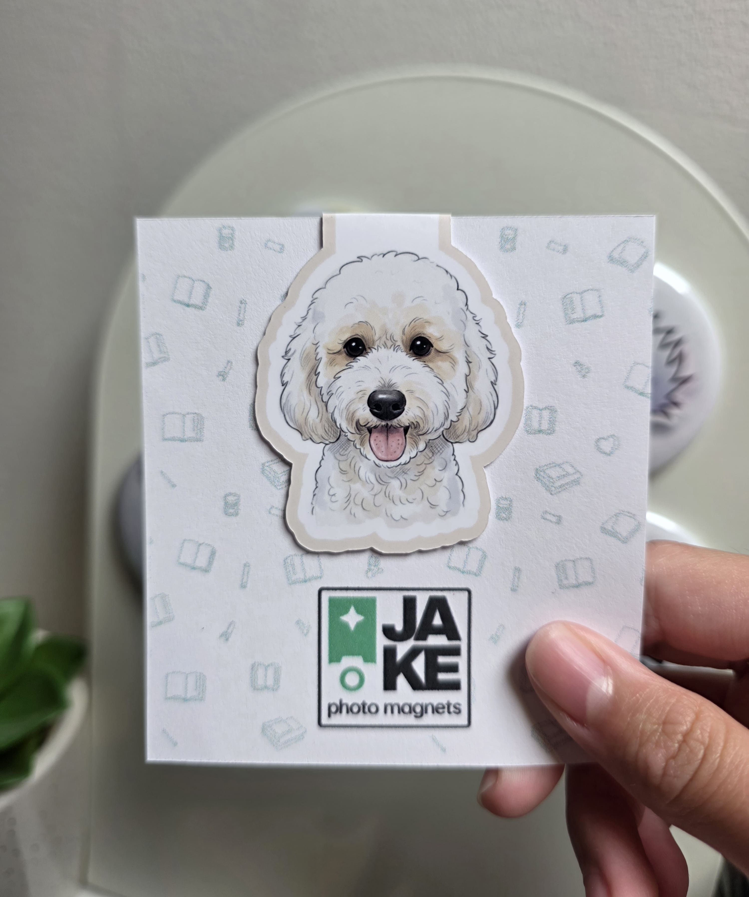 Card with a dog illustration and 'JAKE photo magnets' branding held by a hand.