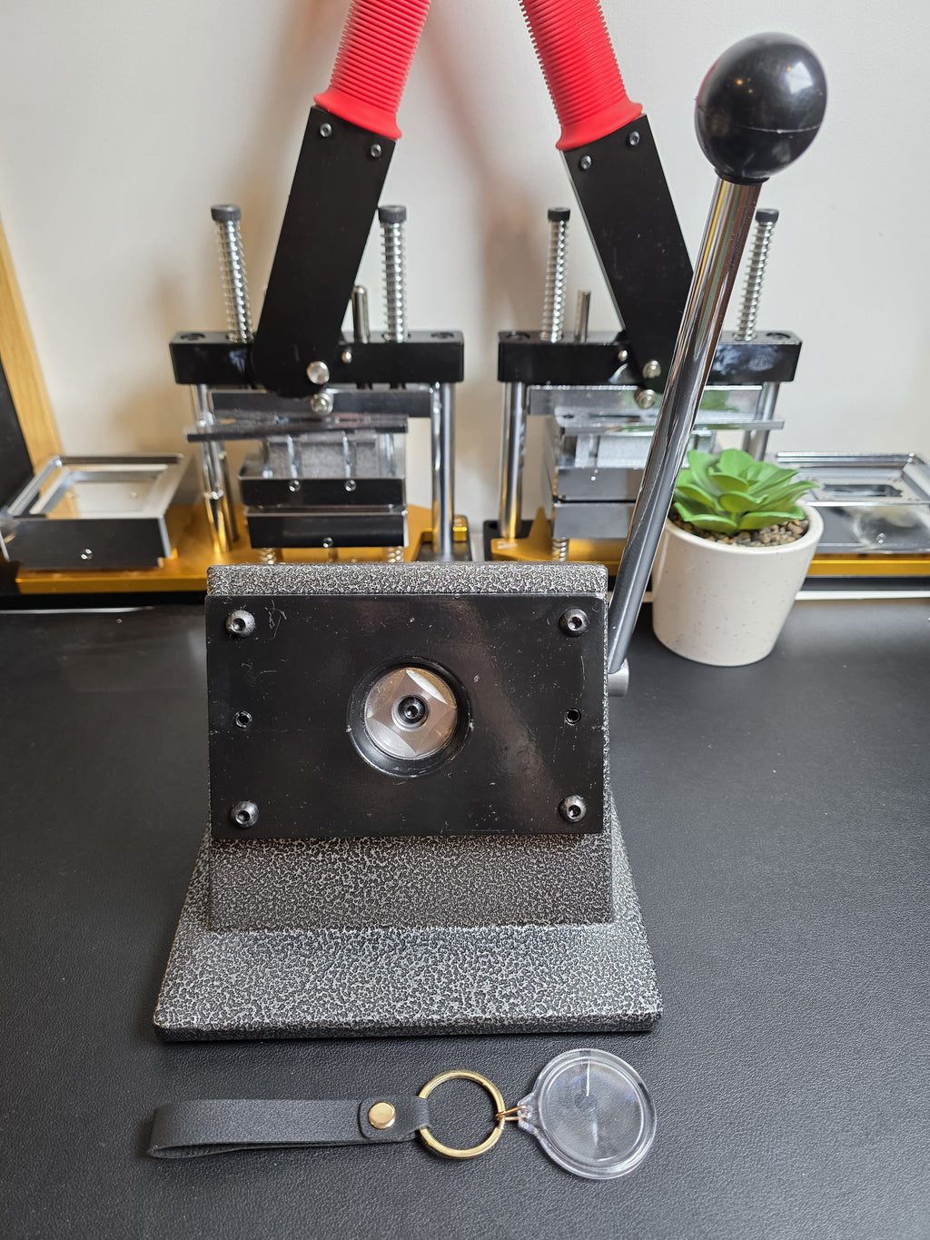 Metal die cutting machine on a gray surface with a plant and keychain in the background