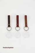 Three clear keychains with brown leather straps on a white background, labeled 'Premium Keychains'.