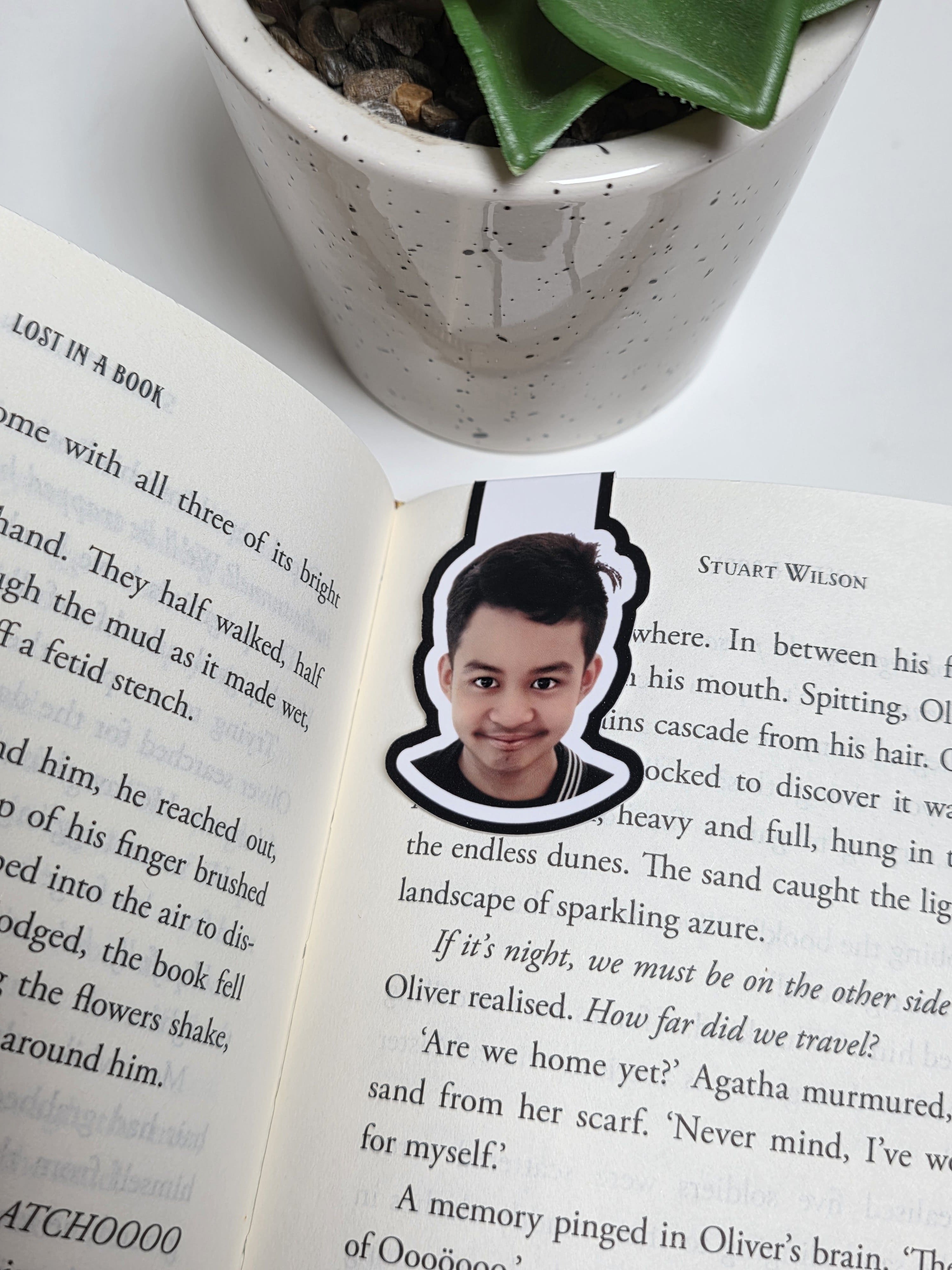 Open book with a sticker of a person's face on a white surface with a plant.