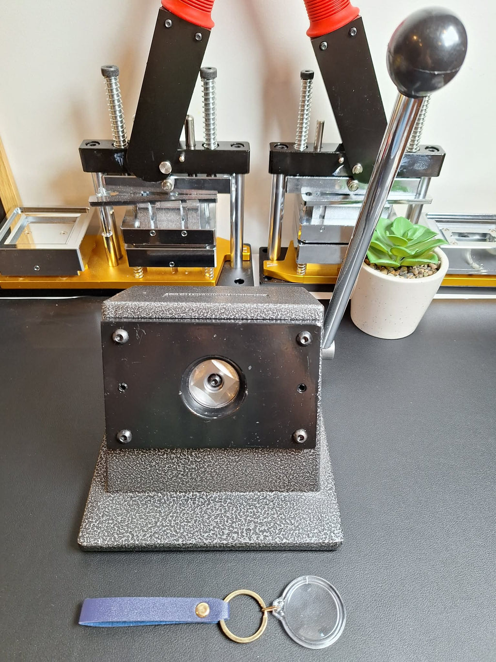 Metal press machine on a gray surface with a keychain and clear plastic sheet