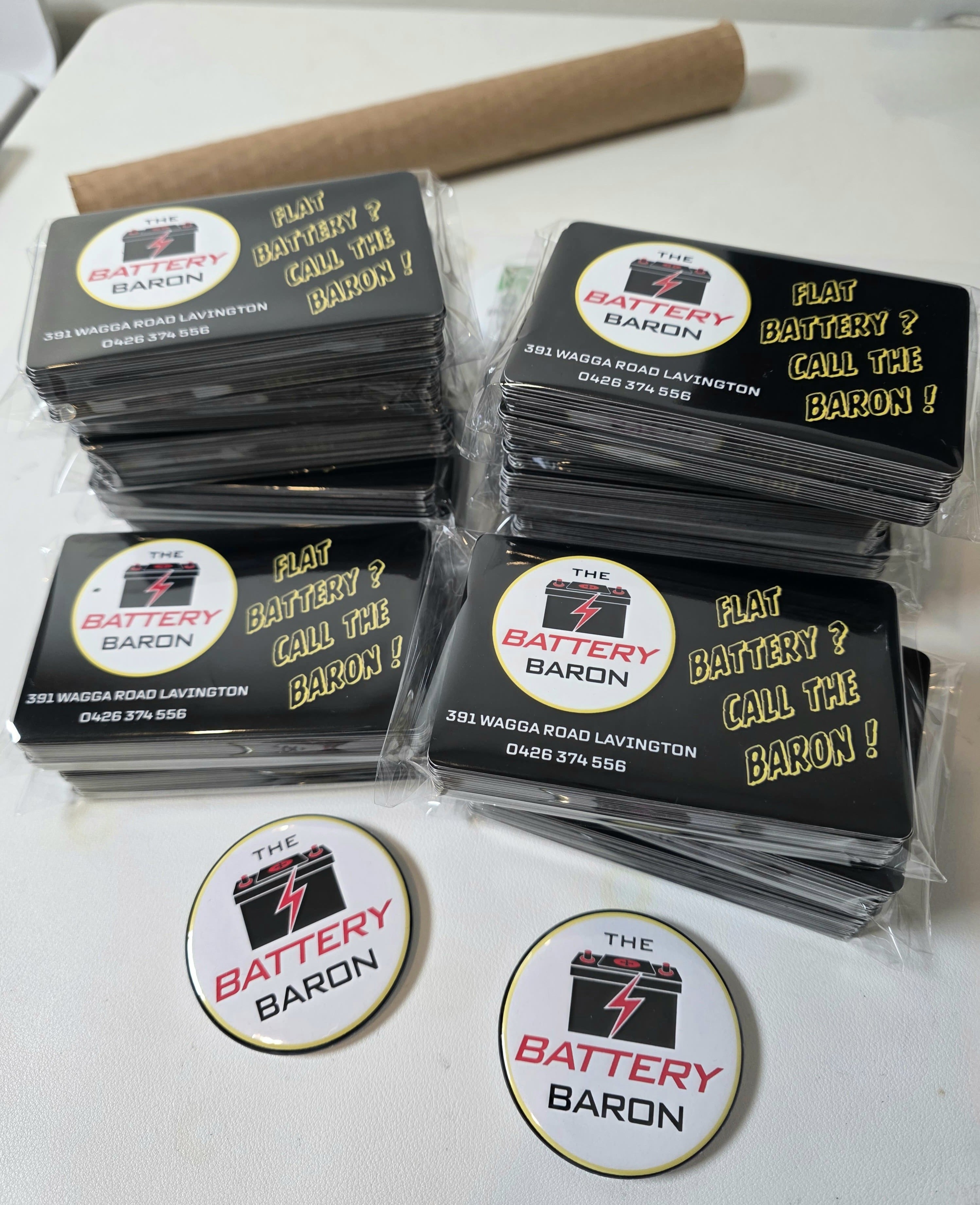 Badges and magnetic business cards for 'The Battery Baron' on a white surface.